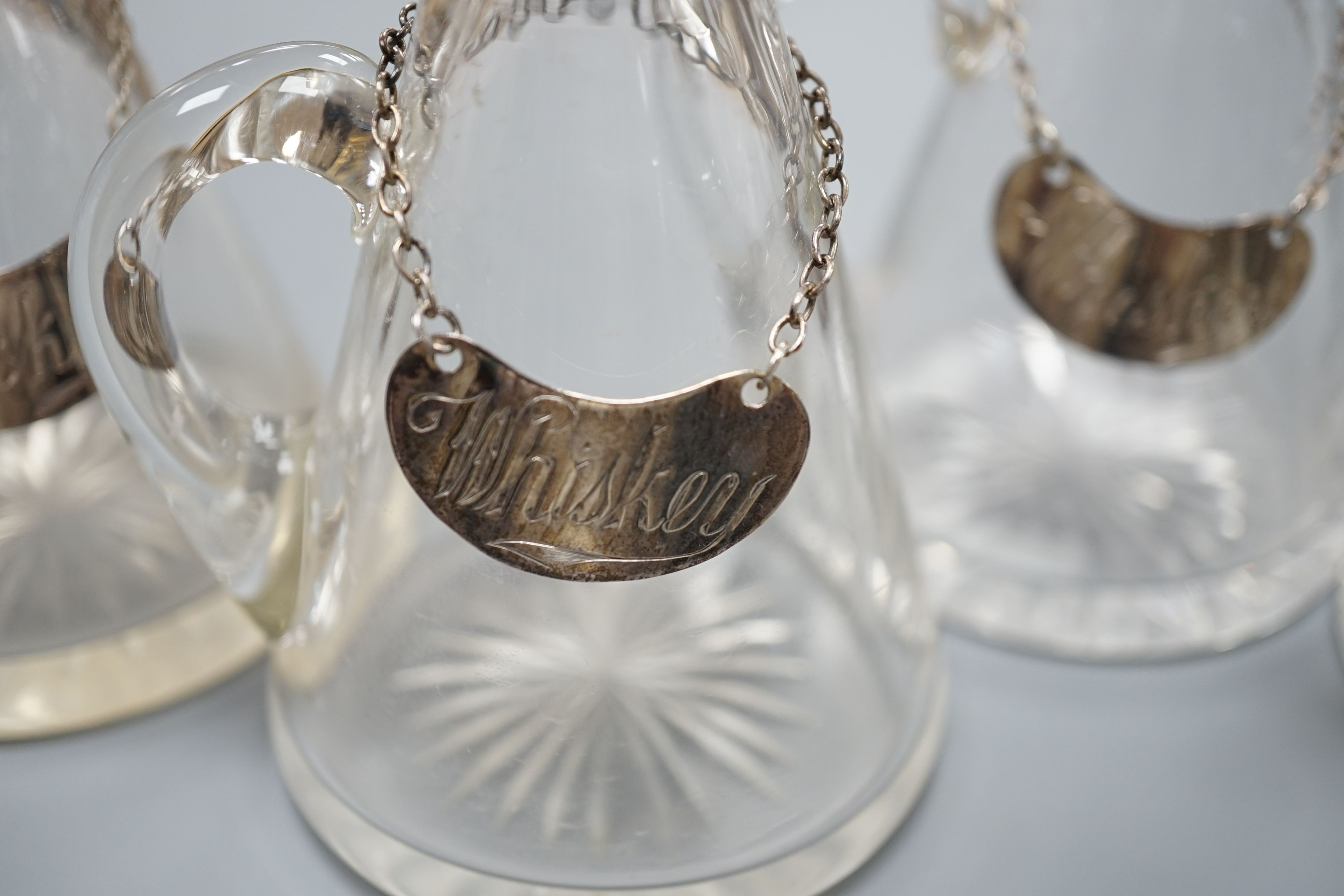 Four silver mounted cut glass whisky tots including a pair by Elkington & Co, 1930, 10.7cm, together with four assorted silver whiskey labels (one thumbpiece missing).